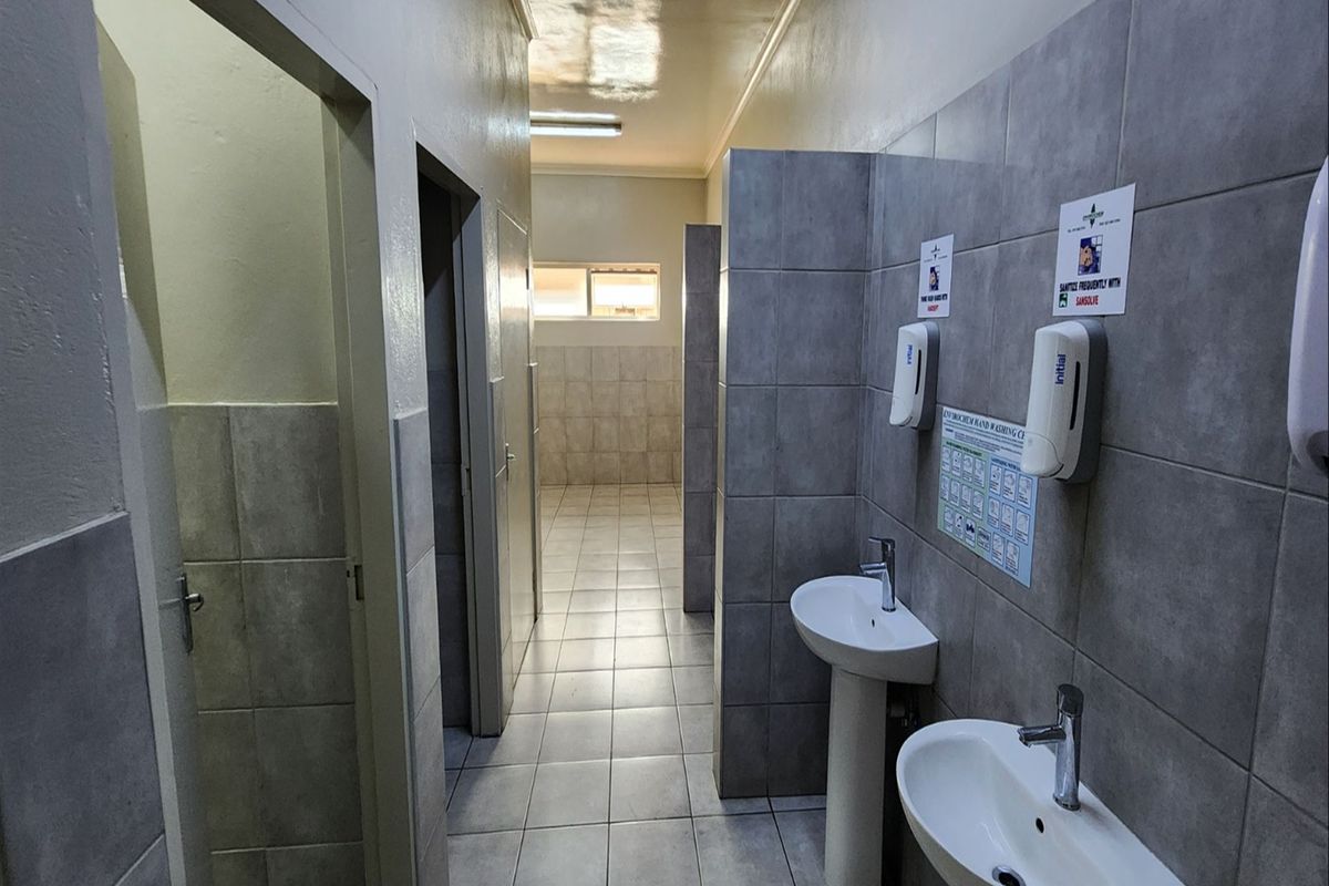 A clean, functional industrial-style communal bathroom featuring tiled walls, pedestal wash basins, and partitioned cubicles.