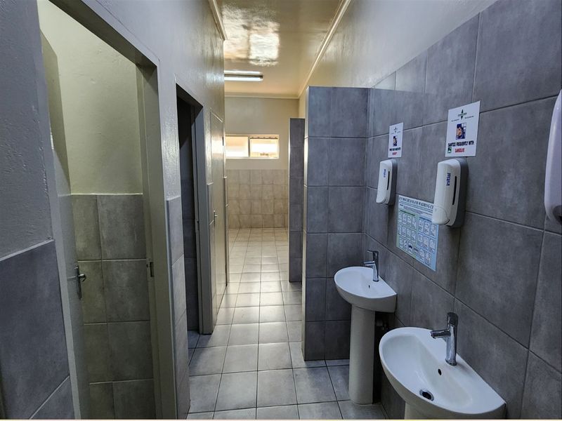 A clean, functional industrial-style communal bathroom featuring tiled walls, pedestal wash basins, and partitioned cubicles.