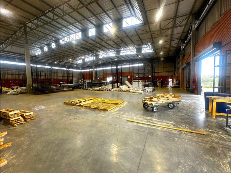 Spacious industrial warehouse featuring high ceilings with exposed steel trusses, skylights for natural light, and durable concrete flooring with large roller shutter access.