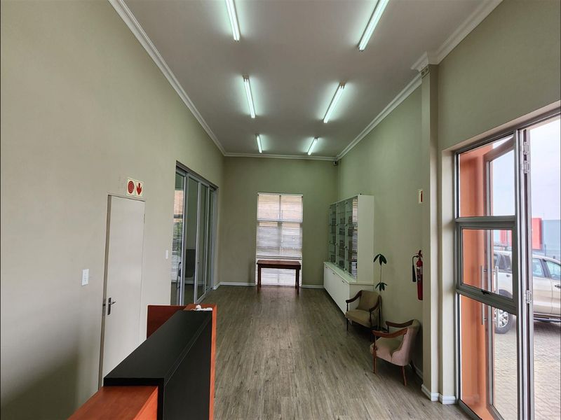 A bright, professional reception or entry area featuring laminate flooring, built-in display cabinetry, and large aluminium-framed glass doors providing natural light.