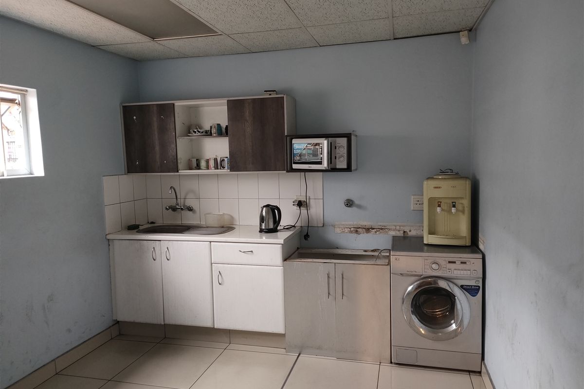 A functional kitchen area featuring built-in cabinetry, a stainless steel sink, and tiled flooring, currently showing signs of wear and requiring cosmetic updates.