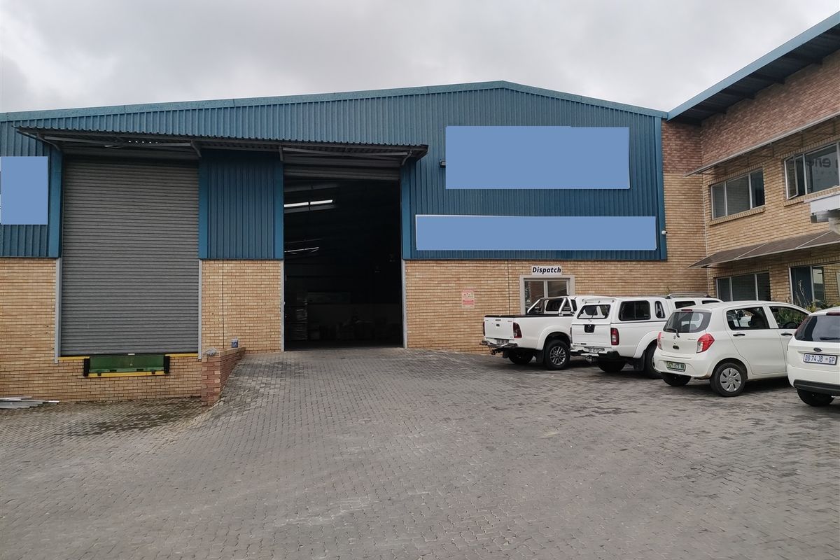 Industrial warehouse exterior featuring a large roller shutter door, loading dock access, and a paved driveway area.