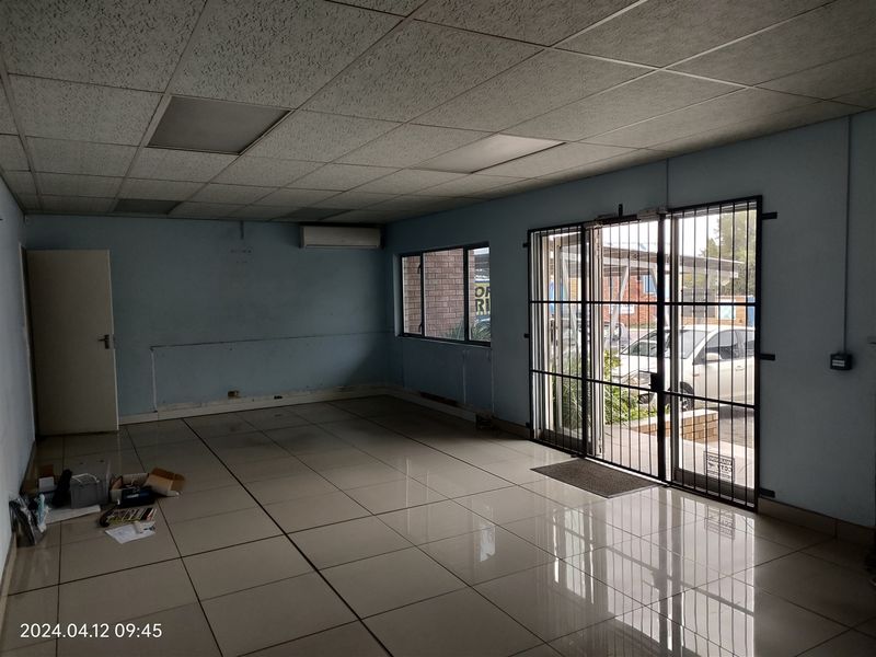 Open-plan office space featuring tiled flooring, a suspended ceiling with recessed lighting, a split-system air conditioner, and secure glass entrance doors.