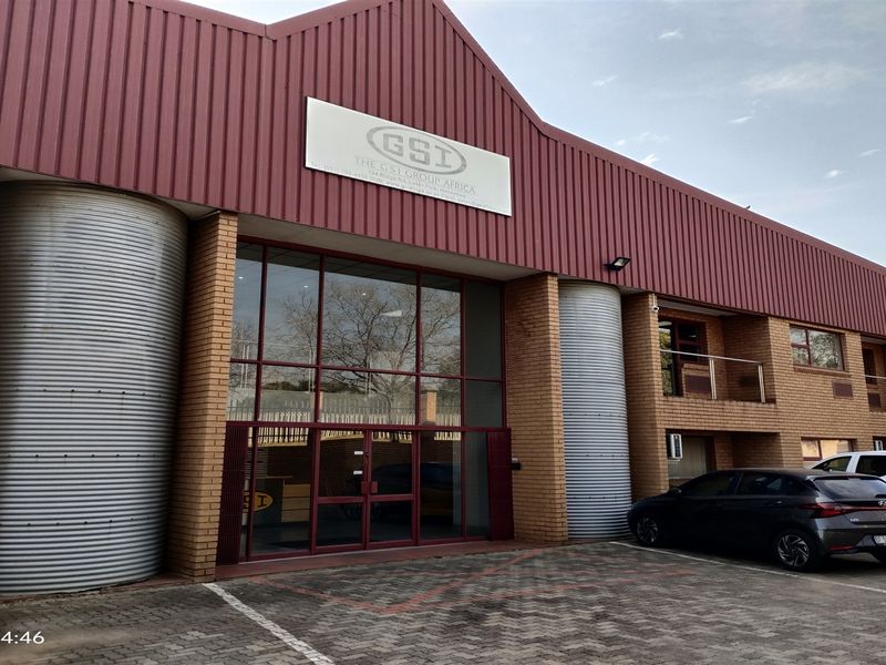 Front elevation of an industrial facility featuring a prominent corrugated metal roof, brick facade, glass entrance, and integrated metal silo structures.