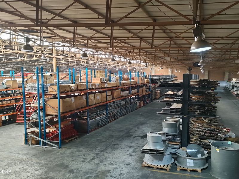 Large industrial warehouse space featuring high exposed steel roof trusses, extensive racking systems, and durable concrete flooring suitable for storage or manufacturing operations.