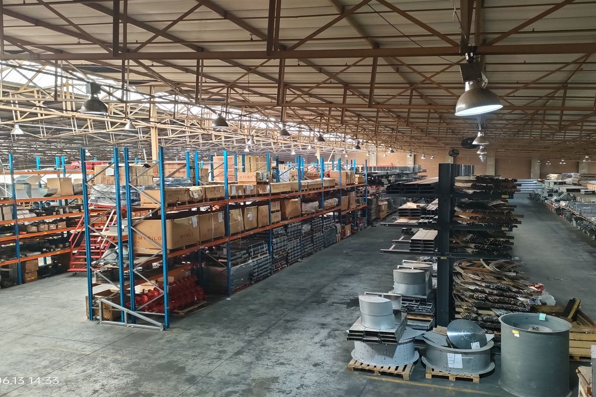 Large industrial warehouse space featuring high exposed steel roof trusses, extensive racking systems, and durable concrete flooring suitable for storage or manufacturing operations.
