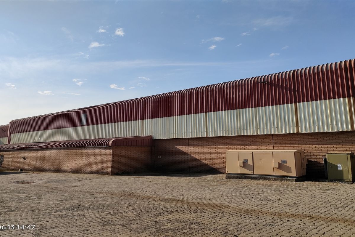 Rear exterior view of an industrial warehouse featuring brick masonry walls, corrugated metal cladding, and a paved yard area with utility enclosures.