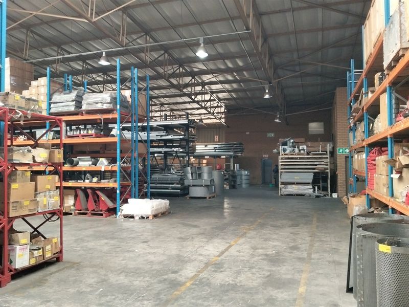 Spacious industrial warehouse featuring high ceilings with exposed steel trusses, concrete flooring, and extensive built-in steel racking systems for storage.