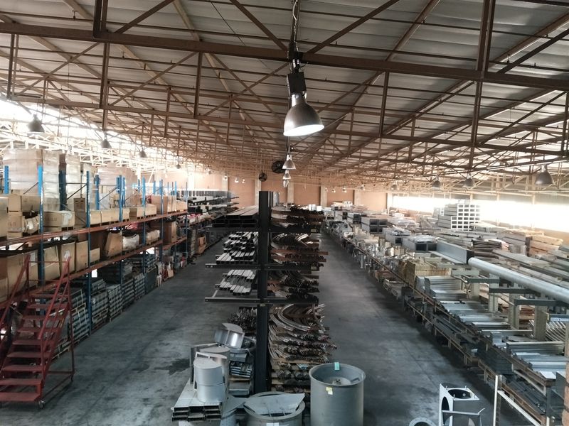 Spacious industrial warehouse featuring high exposed steel roof trusses, concrete flooring, and extensive integrated racking systems for storage and operational use.