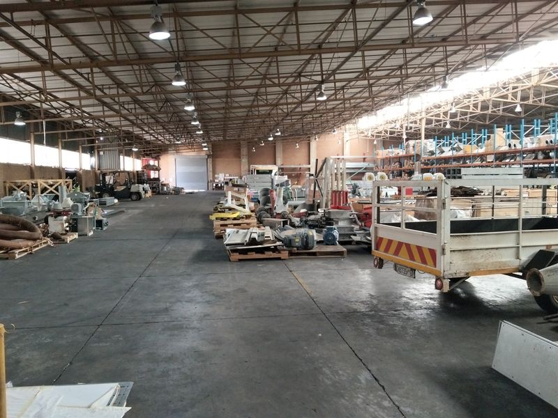 Spacious industrial warehouse featuring high-clearance steel truss roofing, concrete flooring, industrial racking systems, and a large roller shutter door for logistics access.