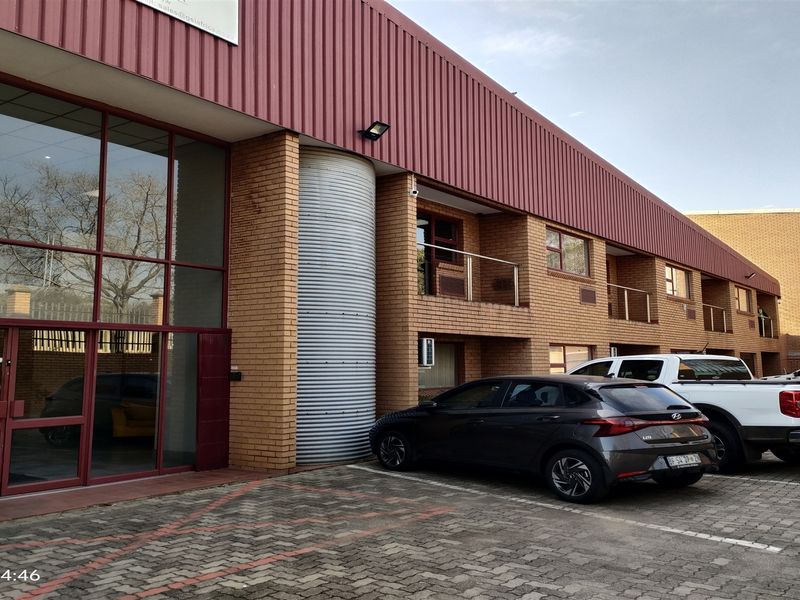 Front elevation of an industrial property featuring a brick facade, large glass entrance, and paved parking area with balcony access.