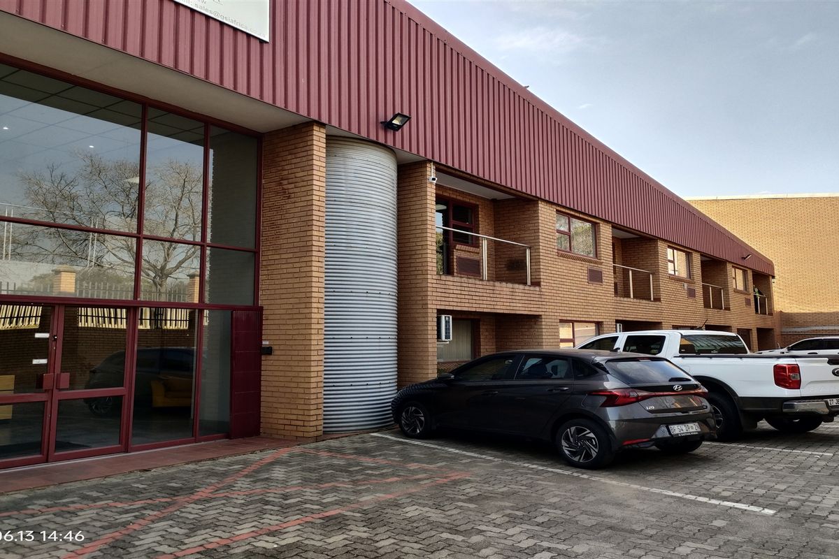 Front elevation of an industrial property featuring a brick facade, large glass entrance, and paved parking area with balcony access.