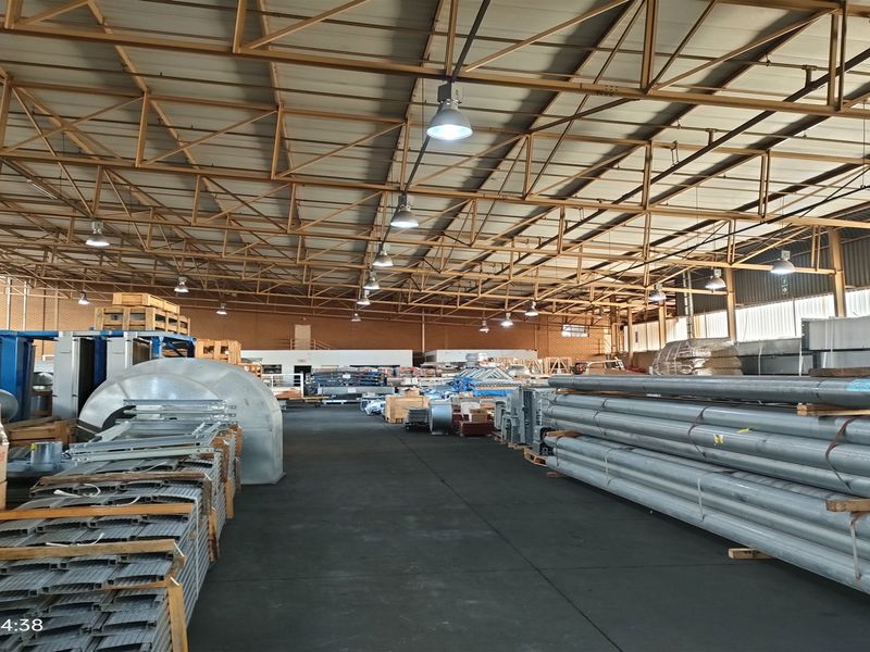Spacious industrial warehouse featuring exposed steel roof trusses, high-bay pendant lighting, and durable concrete flooring, suitable for storage or manufacturing operations.
