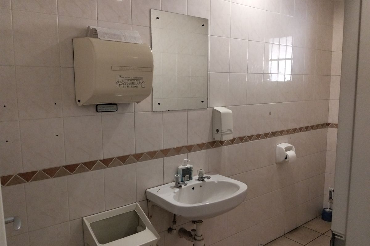 A functional industrial bathroom featuring tiled walls and flooring, a wall-mounted basin, and essential utility dispensers.
