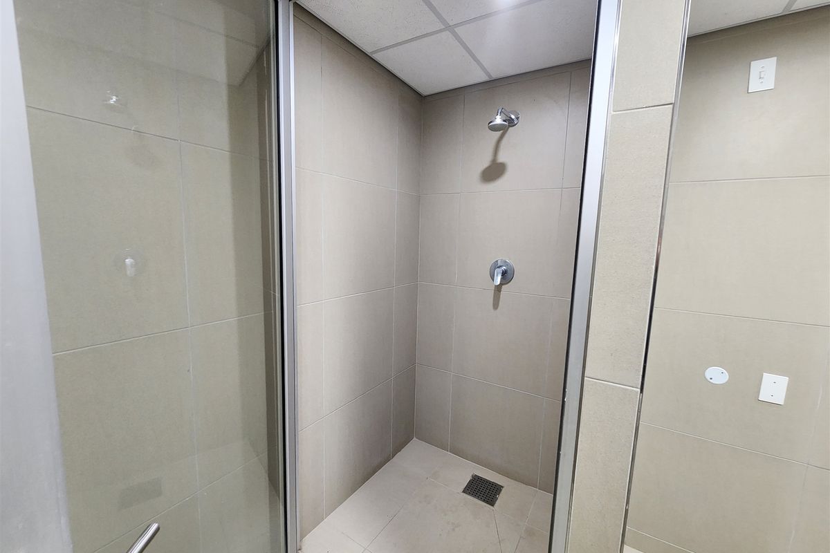 A clean, modern shower stall featuring neutral wall and floor tiling, a glass enclosure, and a drop ceiling with integrated lighting.