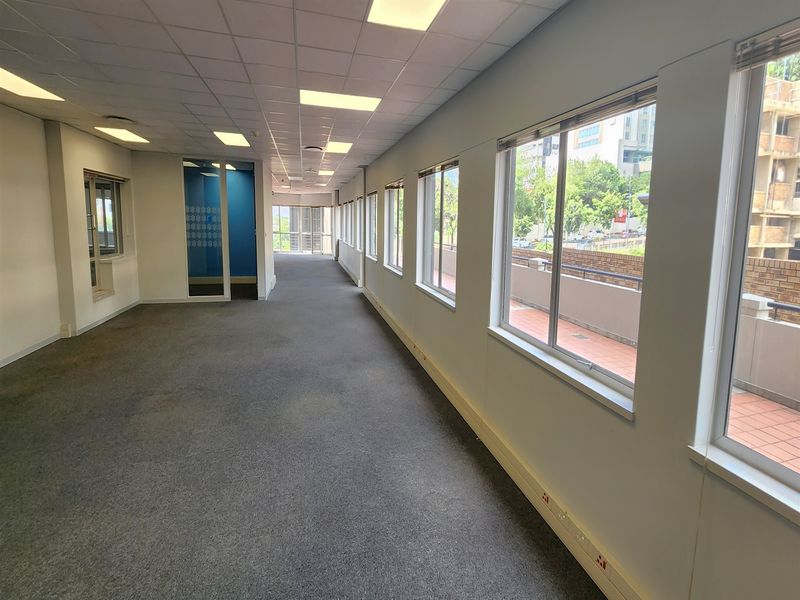 Spacious, open-plan office area featuring large windows, suspended ceilings with recessed lighting, and carpeted flooring, offering a bright and functional workspace.