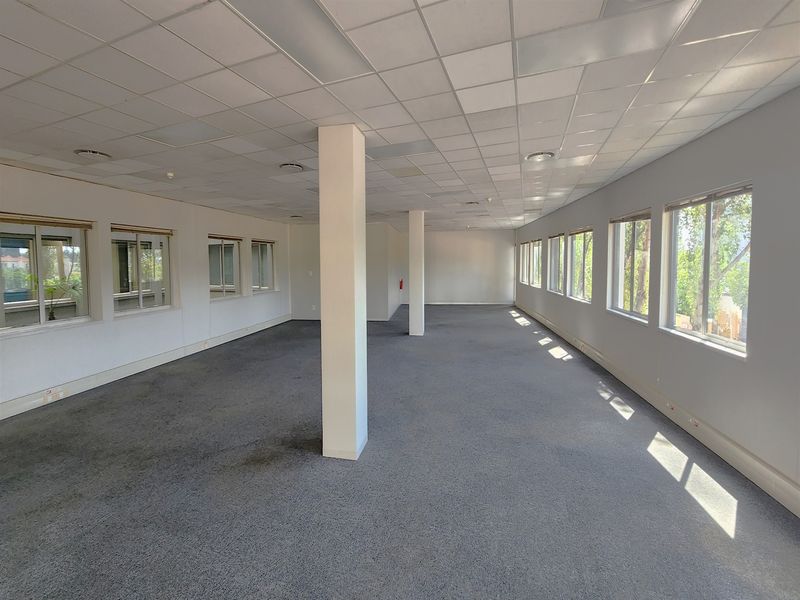 A spacious, open-plan office area featuring a suspended ceiling, structural columns, and large windows providing ample natural light.