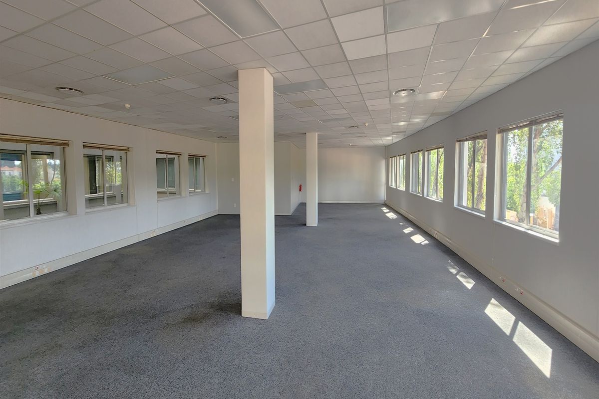 A spacious, open-plan office area featuring a suspended ceiling, structural columns, and large windows providing ample natural light.