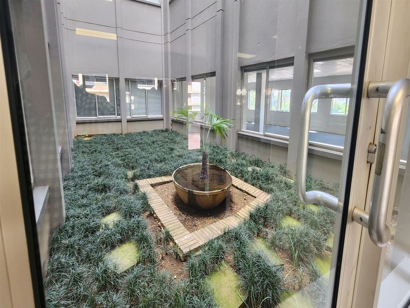 A central office courtyard featuring a brick planter and landscaped ground cover, viewed through a glass entrance door.