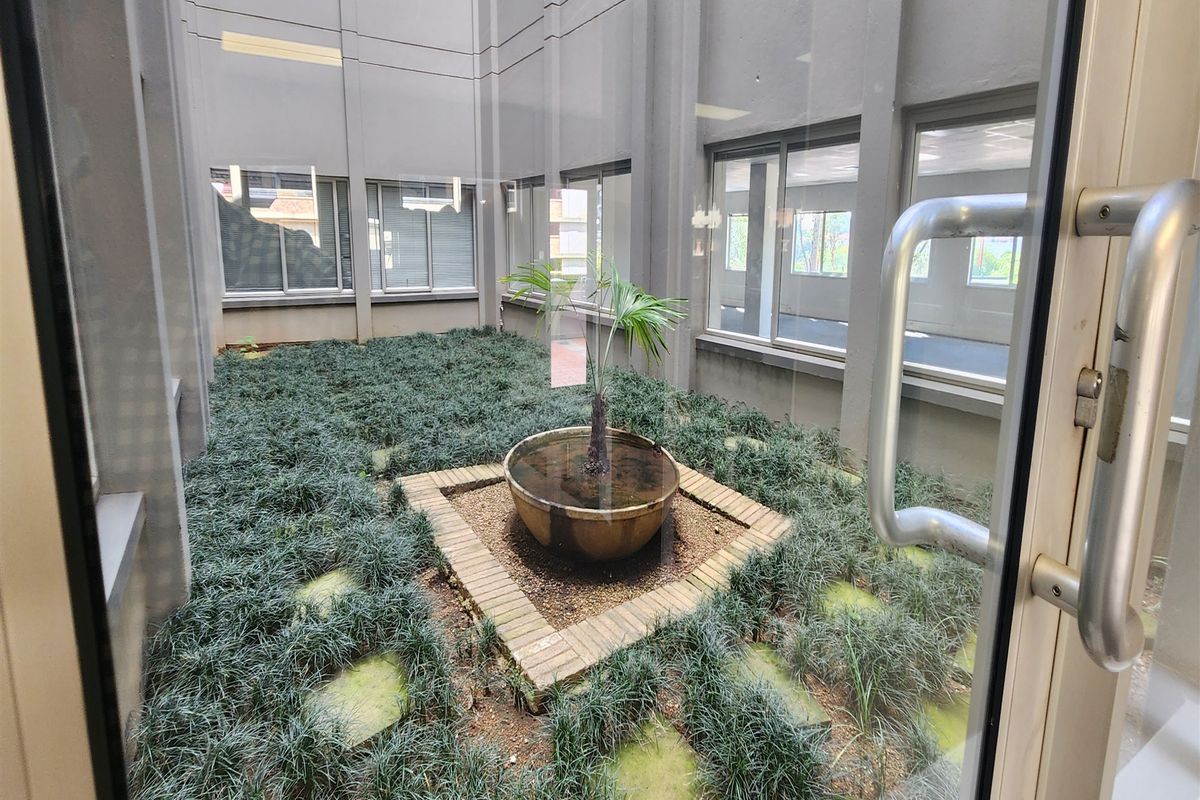 A central office courtyard featuring a brick planter and landscaped ground cover, viewed through a glass entrance door.