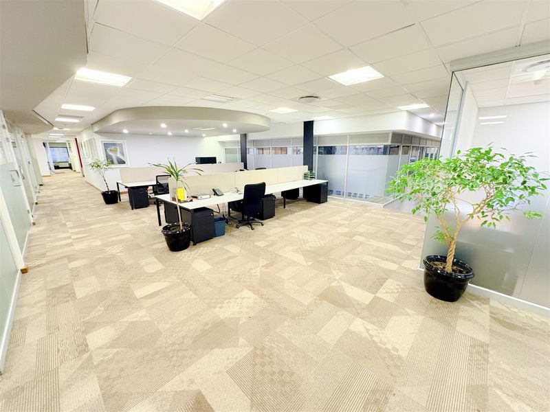 A modern open-plan office space featuring carpeted flooring, suspended ceilings with recessed lighting, and glass partitioning for a professional and bright work environment.