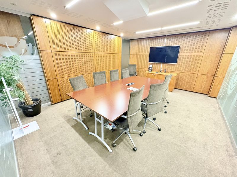 A professional office meeting room featuring acoustic wood wall paneling, recessed linear lighting, and glass partitions, providing a clean and functional workspace.