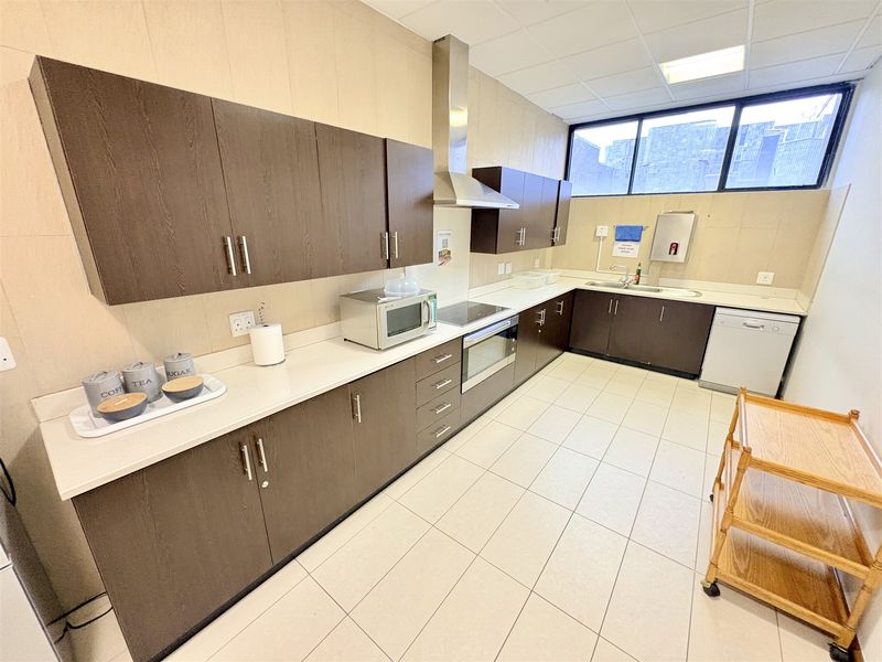 A functional office kitchen featuring dark wood cabinetry, integrated appliances including an oven and extractor fan, and durable tiled flooring.