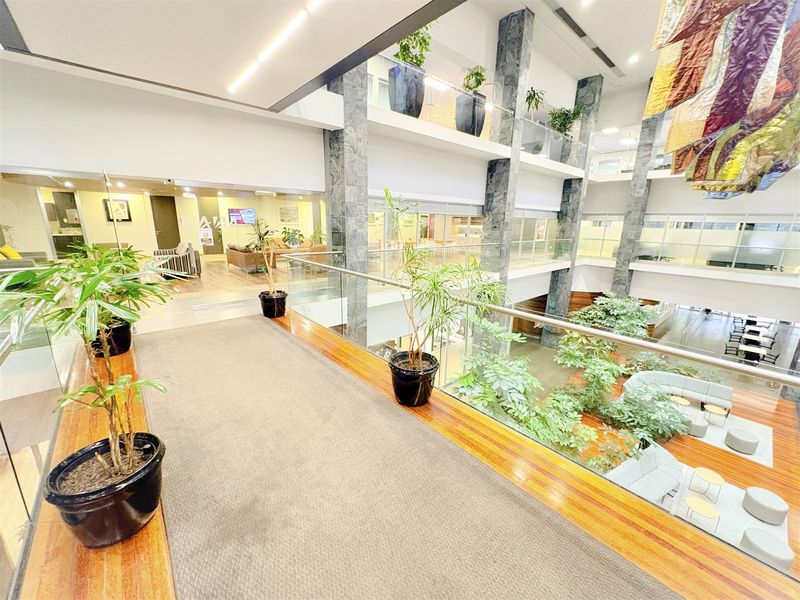 A modern multi-level office atrium featuring stone-clad columns, glass balustrades, and an open-plan design with views into the lower lobby area.