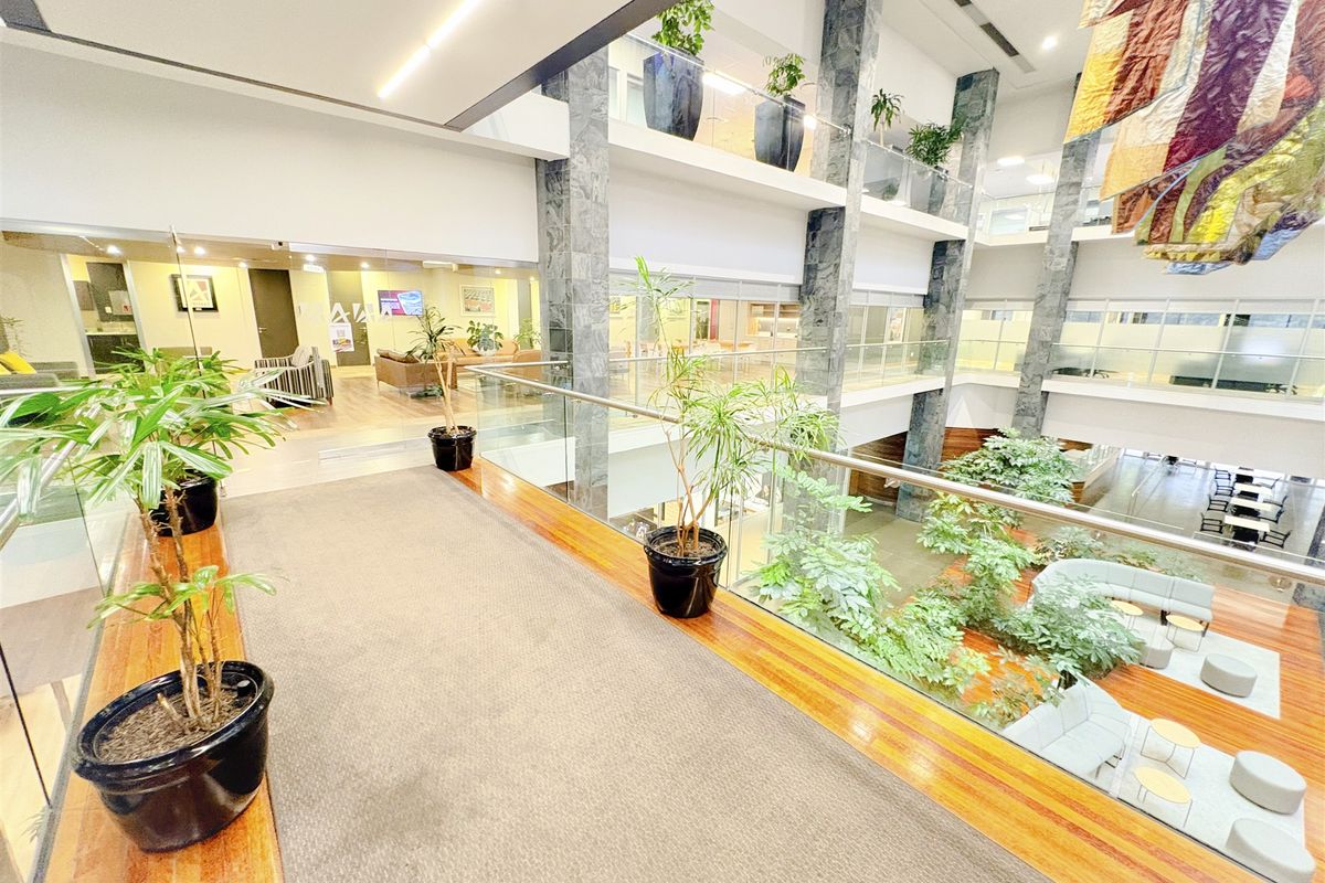 A modern multi-level office atrium featuring stone-clad columns, glass balustrades, and an open-plan design with views into the lower lobby area.