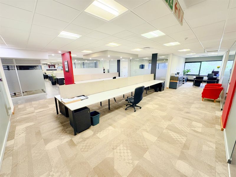Open-plan office space featuring modular desk workstations, glass partitioning, suspended ceilings with recessed lighting, and durable carpet tile flooring.