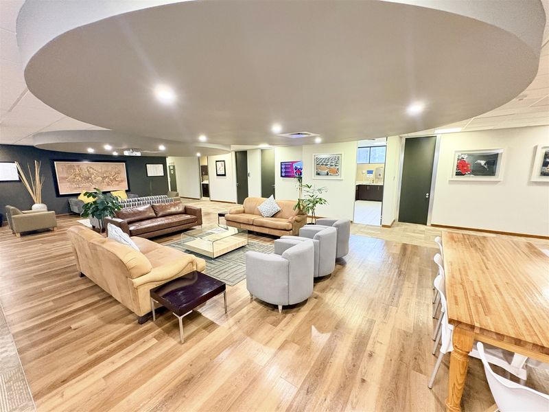 Spacious open-plan office lounge area featuring modern laminate wood flooring, a distinctive circular recessed ceiling detail, and integrated recessed lighting throughout.