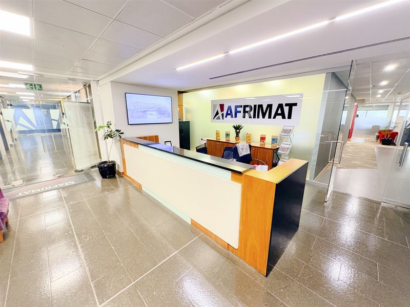 Professional office reception area featuring a modern built-in desk, glass partitioning, and clean tiled flooring in a well-lit corporate environment.