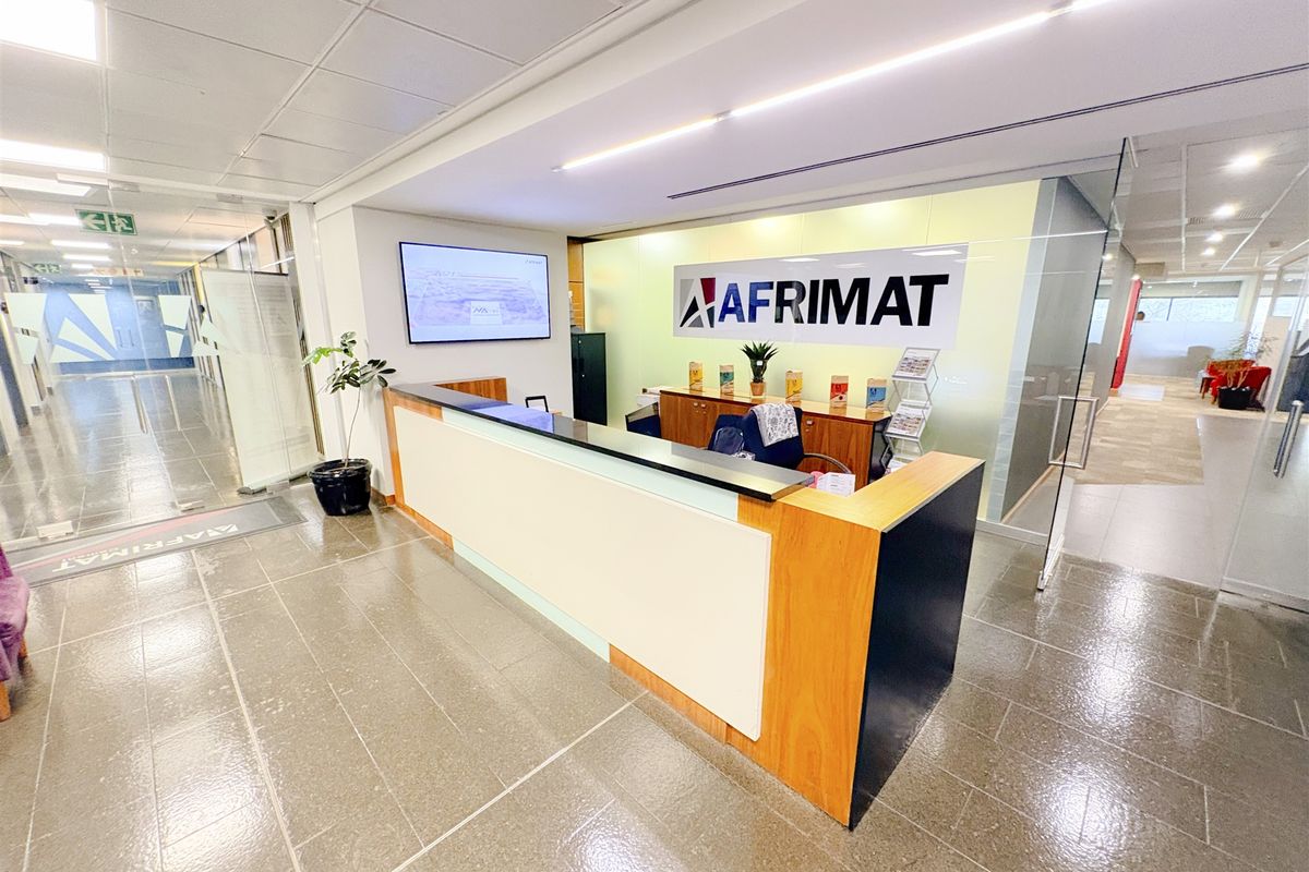 Professional office reception area featuring a modern built-in desk, glass partitioning, and clean tiled flooring in a well-lit corporate environment.