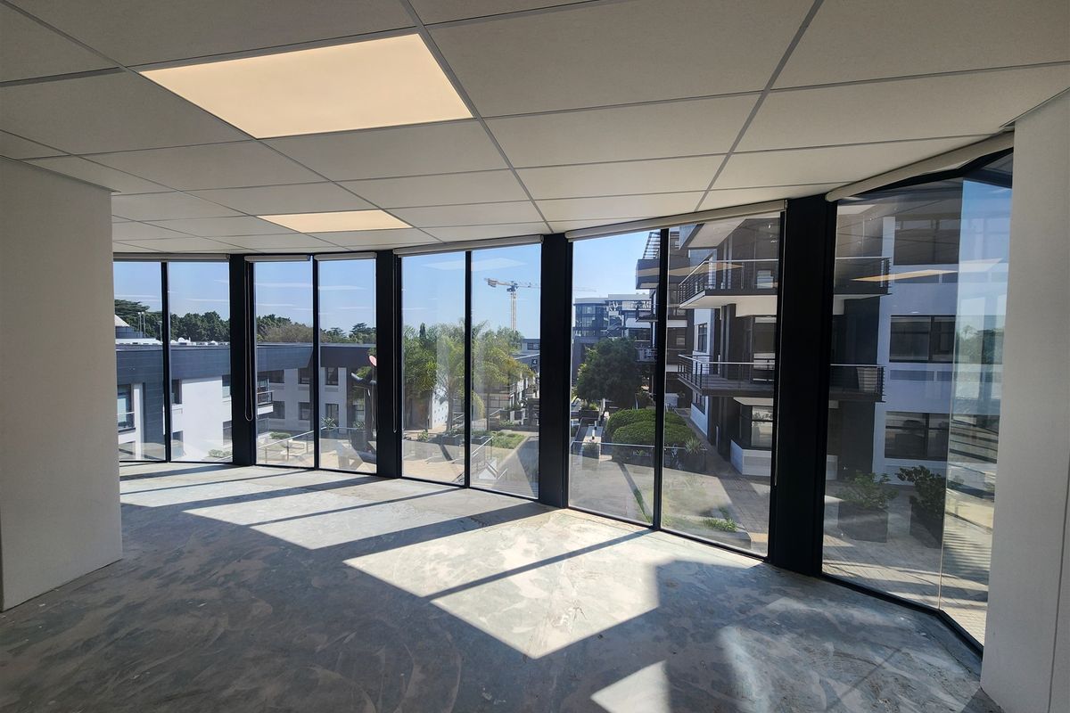 A bright, open-plan office space featuring floor-to-ceiling windows with neighborhood views, a suspended ceiling, and unfinished concrete flooring ready for final finishes.
