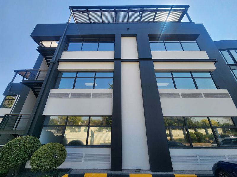 Modern multi-story office building facade featuring large glass windows, clean architectural lines, and a top-level louvered roof structure.