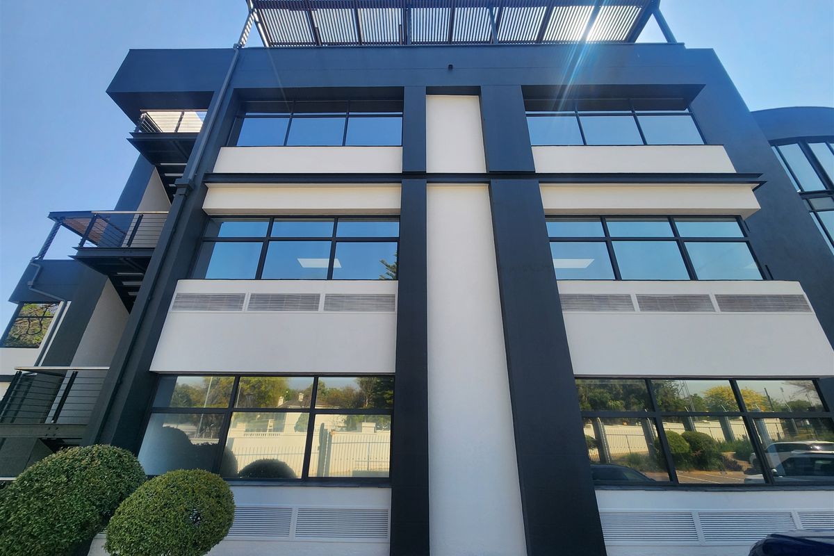 Modern multi-story office building facade featuring large glass windows, clean architectural lines, and a top-level louvered roof structure.