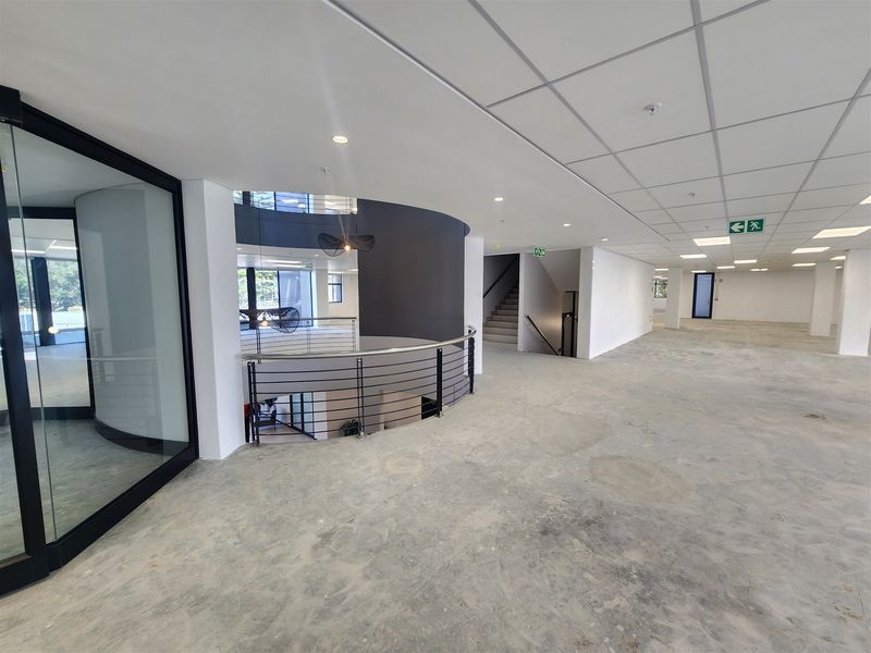 Spacious open-plan office area featuring a modern curved design, suspended ceiling, and a central staircase with metal balustrades, currently in shell condition.