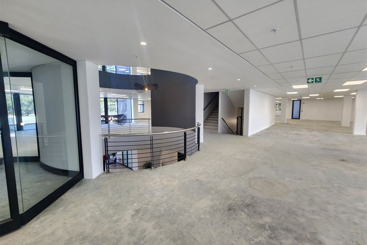 Spacious open-plan office area featuring a modern curved design, suspended ceiling, and a central staircase with metal balustrades, currently in shell condition.