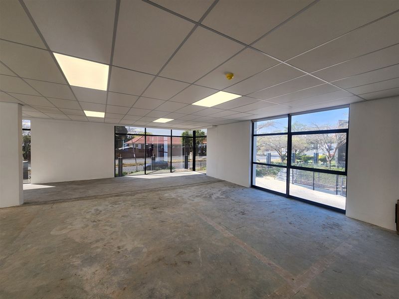 An open-plan office space featuring a suspended ceiling with recessed lighting and large floor-to-ceiling windows providing ample natural light.