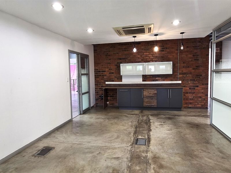 Modern office space featuring an exposed brick feature wall, polished concrete flooring, built-in cabinetry, and glass partitions with integrated ceiling air conditioning.