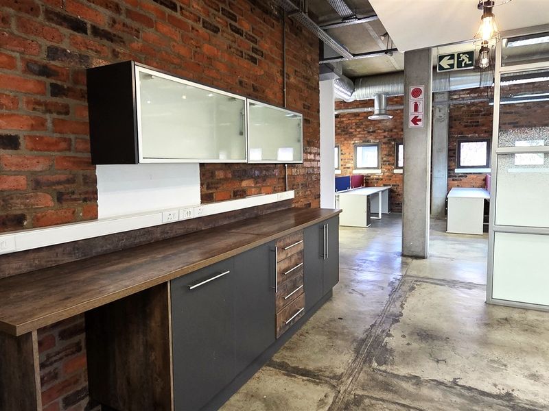 Modern industrial-style office space featuring exposed brick walls, polished concrete floors, built-in cabinetry, and glass partitions with exposed ceiling ducting.