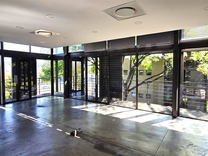 Spacious modern office area featuring polished concrete floors, exposed brick accents, and expansive floor-to-ceiling windows providing ample natural light and balcony access.