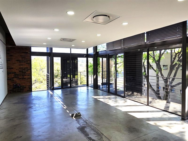 Modern open-plan office space featuring polished concrete floors, exposed brick accents, and expansive floor-to-ceiling windows with integrated balcony access.