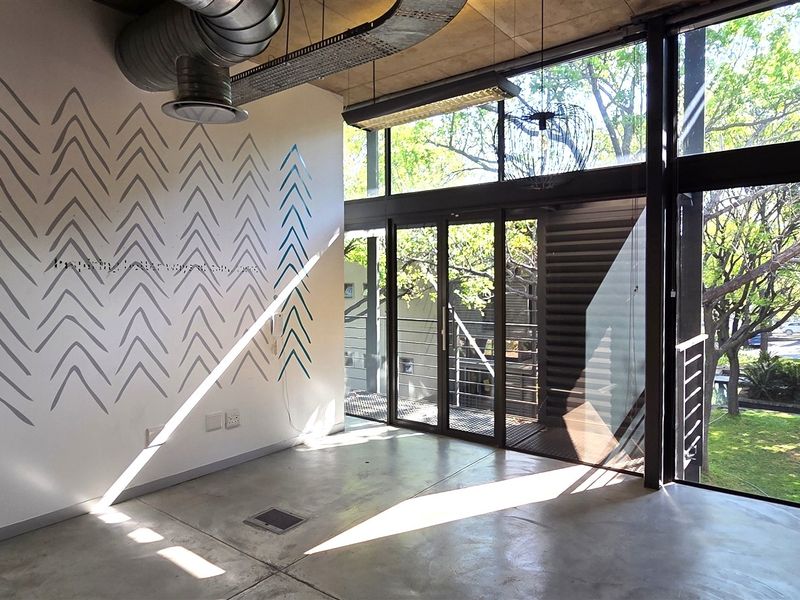 Modern office space featuring polished concrete floors, exposed industrial ducting, and floor-to-ceiling windows providing ample natural light and garden views.