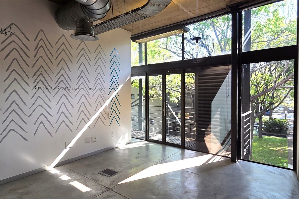 Modern office space featuring polished concrete floors, exposed industrial ducting, and floor-to-ceiling windows providing ample natural light and garden views.