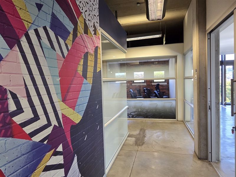 Modern office hallway featuring polished concrete floors, exposed industrial ceiling, glass partitions, and a vibrant painted brick feature wall.
