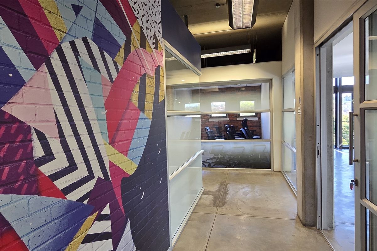 Modern office hallway featuring polished concrete floors, exposed industrial ceiling, glass partitions, and a vibrant painted brick feature wall.