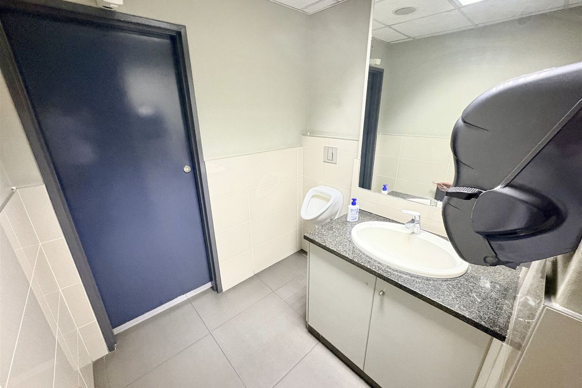A clean, functional office restroom featuring a vanity with a granite countertop, drop-in sink, wall-mounted mirror, and a wall-mounted urinal.