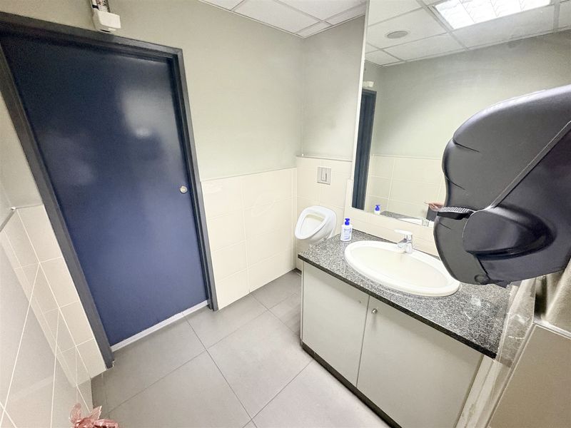 A clean, functional office restroom featuring a vanity with a granite countertop, drop-in sink, wall-mounted mirror, and a wall-mounted urinal.