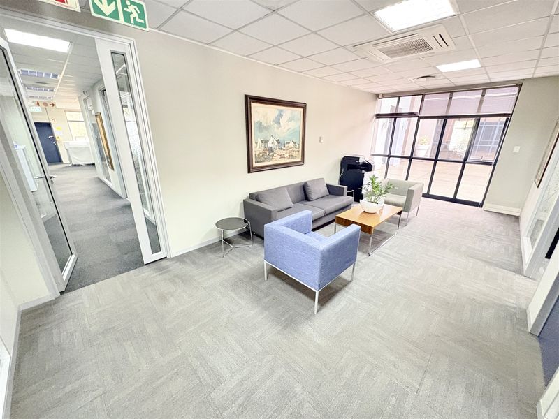 A professional office reception or waiting area featuring carpet tiles, suspended ceilings, and glass partition walls with natural light.
